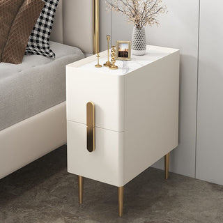 White bedside cabinet with gold handle and legs beside a bed
