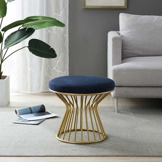 Navy upholstered pouf on a gold wire iron base beside a sofa and a plant