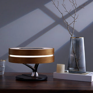 Round wooden tree desk lamp glowing on a dark desk beside a glass vase