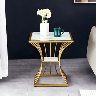 Gold-framed tempered glass side table with flowers and a mug against a dark wall