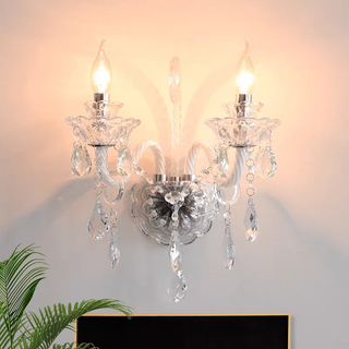 Crystal candle-style wall sconce with flame-shaped bulbs glowing on a wall