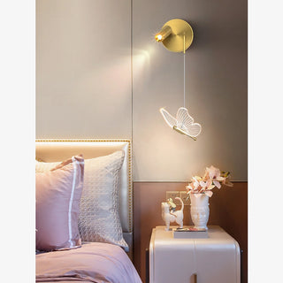 Nursery corner with a brass and butterfly wall lamp above a crib-side table with soft pink bedding by Mirodemi