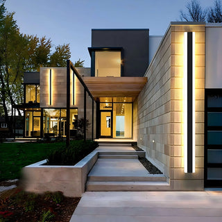 Modern home facade lit with vertical linear uplights along the entrance wall at dusk