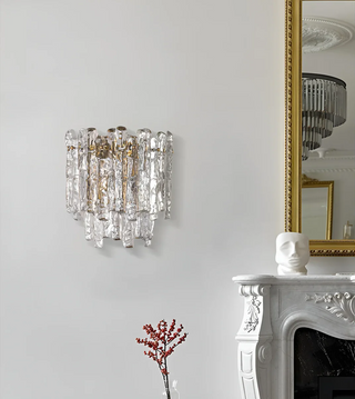 Crystal wall sconce mounted beside a gold-framed mirror above a marble mantel