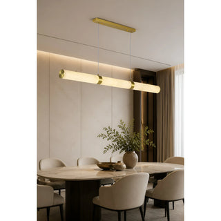 Linear alabaster pendant light glowing over a dining table with beige chairs