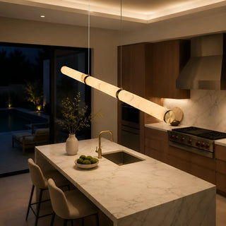 Linear pendant light hanging over a kitchen island with a sink and marble countertop