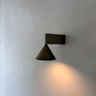 Black Bauhaus aluminum cone wall lamp glowing on a plain wall