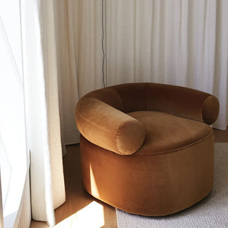 Rust velvet single-seat sofa beside a sheer curtain