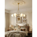 A stylish brass chandelier with white glass spheres lighting up a cozy bedroom space, hanging from a decorative ceiling medallion