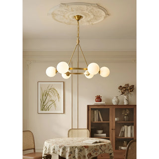 A brass chandelier with white milk glass spheres installed in a cozy dining room, complementing the home decor