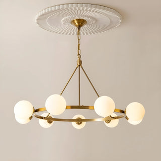 A brass chandelier with six white milk glass spheres, suspended from an elegant ceiling medallion