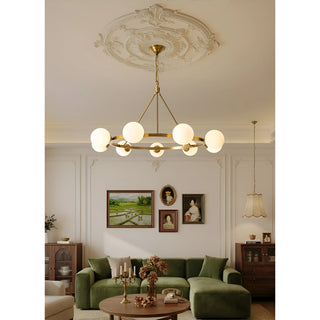 A brass chandelier with white glass spheres suspended from a decorative ceiling medallion, illuminating a cozy living room with green furniture