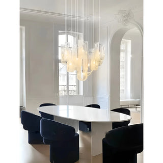 Modern glass chandelier hanging above a dining table with dark chairs in a minimalist interior