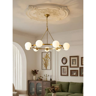 A stylish brass chandelier with glass spheres hanging from a decorative ceiling medallion in a bright and airy living room
