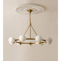 Full view of the brass chandelier with six white milk glass spheres, suspended from a classic ceiling medallion