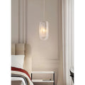 Single modern pendant light with textured U-shaped glass shade hanging beside a bed in a neutral bedroom interior