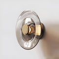Modern glass disc wall sconce with gold metal base and warm LED lighting