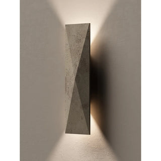 Modern wall sconce made of natural travertine, casting warm up and down light on a textured wall in minimalist design.