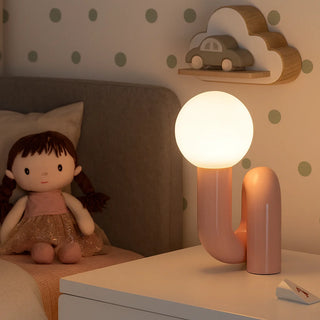 Pink resin bedside lamp with glass globe in children’s bedroom – playful modern design night light