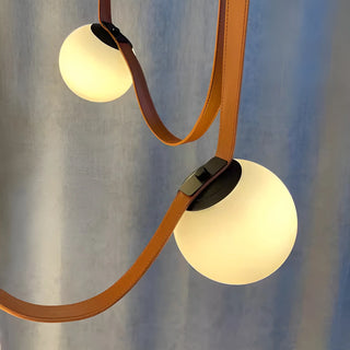 Detail shot of Scandinavian pendant chandelier showing leather straps and matte glass globes with soft lighting