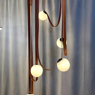 Close-up view of Scandinavian chandelier with brown leather straps and frosted glass globes emitting warm light
