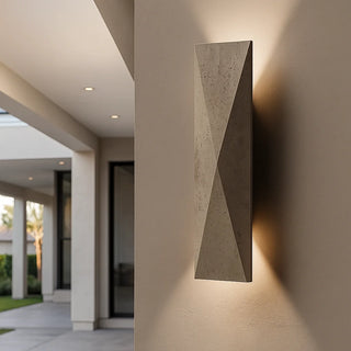 Modern photograph of a travertine wall light mounted on the exterior wall of a minimalist American home, glowing warmly in the evening