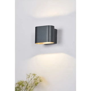 Aeris black wall sconce softly glowing with dual beam in daylight setting