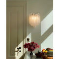 Elegant clear textured glass wall sconce mounted in a sunlit interior beside floral decor and warm natural shadows