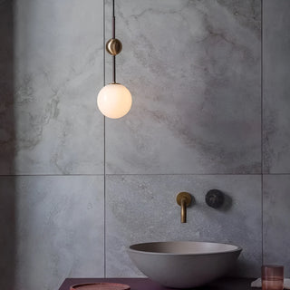Frosted globe pendant light suspended over a modern sink in a concrete-tiled bathroom