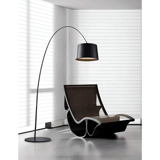 Modern black arc floor lamp positioned beside sculptural lounge chair in bright minimalist space