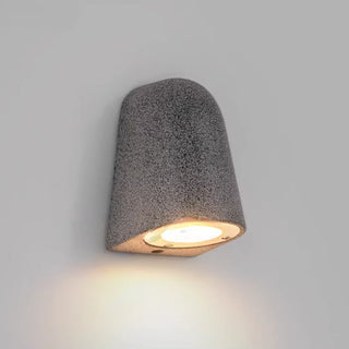 Black sandstone microcement wall light with warm illumination against minimalist backdrop