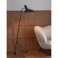 Minimalist black tripod floor lamp next to armchair in modern bedroom interior