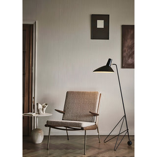 Black modern tripod floor lamp next to lounge chair in stylish reading corner