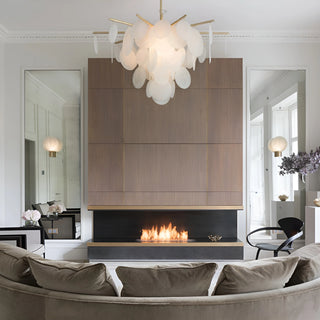 Brass chandelier with layered glass discs illuminating a contemporary living room with fireplace and wood panel accents