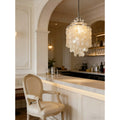 Capiz shell chandelier hanging over a white marble bar with beige upholstered bar stool, showcasing luxury interior lighting design
