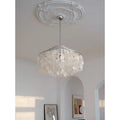 Elegant capiz shell chandelier hanging from ornate white ceiling medallion with modern abstract and floral wall art in a bright living room