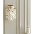 Gold Capiz Shell Wall Sconce mounted on a decorative wall, creating a soft ambient glow with cascading shell discs