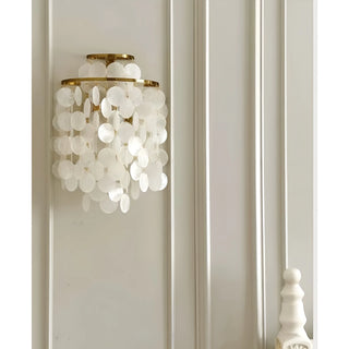 Gold Capiz Shell Wall Sconce mounted on a decorative wall, creating a soft ambient glow with cascading shell discs