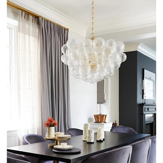 Modern round glass chandelier with gold finish installed above black dining table.