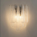 Detailed close-up of a handcrafted textured glass wall sconce with layered clear glass elements and warm ambient lighting