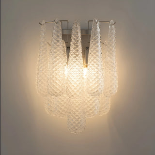 Detailed close-up of a handcrafted textured glass wall sconce with layered clear glass elements and warm ambient lighting
