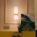 Double glossy white glass wall sconce with brushed brass base mounted on a warm beige wall in a modern interior