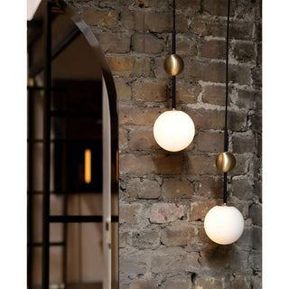 Two globe pendant lights with brass details mounted against an exposed brick wall