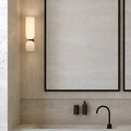 Double glossy white glass wall sconce mounted on a textured bathroom wall above a sink