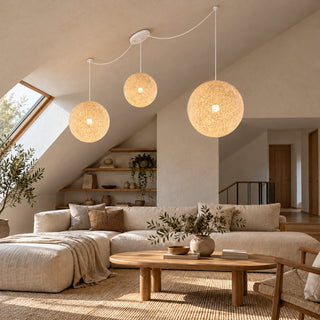 Filara three-light woven globe pendant with white cords mounted on a sloped ceiling above a neutral living room