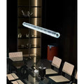 Illuminated glass tube pendant light suspended above a modern dining table with rattan chairs and glass cabinet in the background
