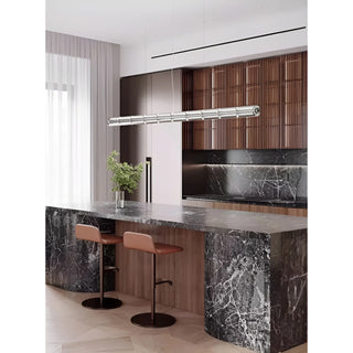 Glass tube pendant light hanging over a marble kitchen island in a sleek, modern interior with wooden cabinetry