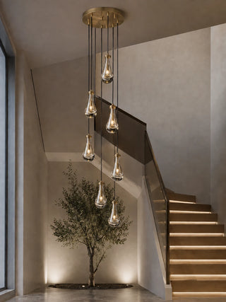 Guttara 7-light raindrop chandelier descending a staircase beside an olive tree