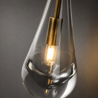 Close-up of a single Guttara glass raindrop with a brass cap and warm E14 filament bulb