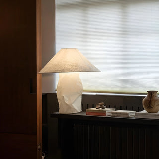 Japandi inspired paper table lamp with sculptural base placed near a window with books in a modern interior